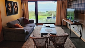 A living room with a sofa, a TV, a table, wicker chairs, and a view through a glass door. - Correntoso TownHouses (Villa La Angostura)