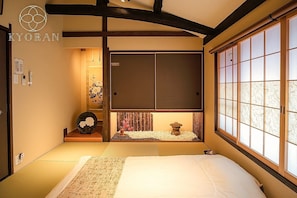 Ein traditioneller japanischer Raum mit Tatami-Boden, niedrigem Bett, einer Schiebetür und einem großen Fenster mit Gartenblick.