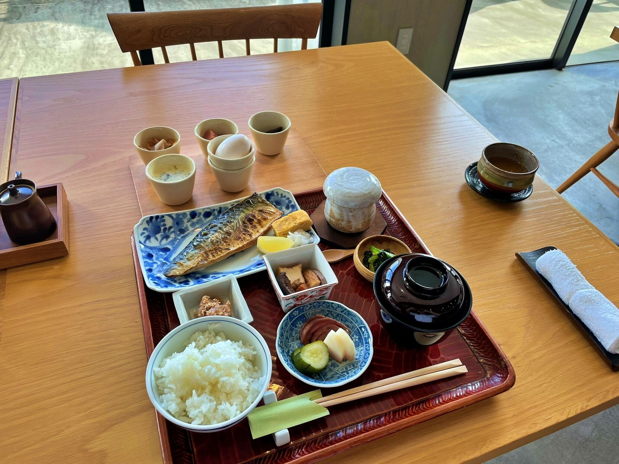 A wooden dining table with a tray containing various dishes, including rice, fish, and vegetables, along with several cups and a teapot.