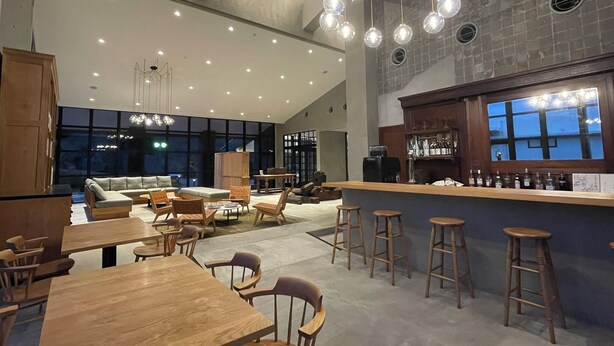 Ein großzügiger Loungebereich mit hohen Decken, eine Bar mit Hockern und eine Sitzecke mit Sofas und Tischen.