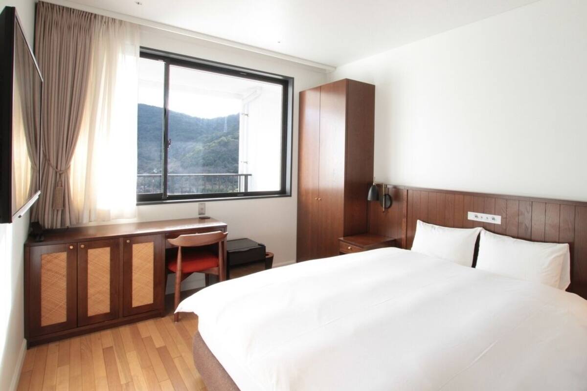 A hotel room with a bed, a desk, a chair, a wardrobe, and a window with a view of the mountains.