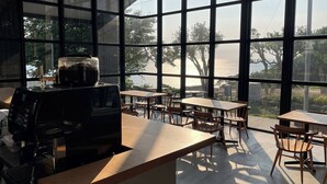 Ein Café mit großen Fenstern, Tischen, Stühlen und einer Kaffeemaschine.