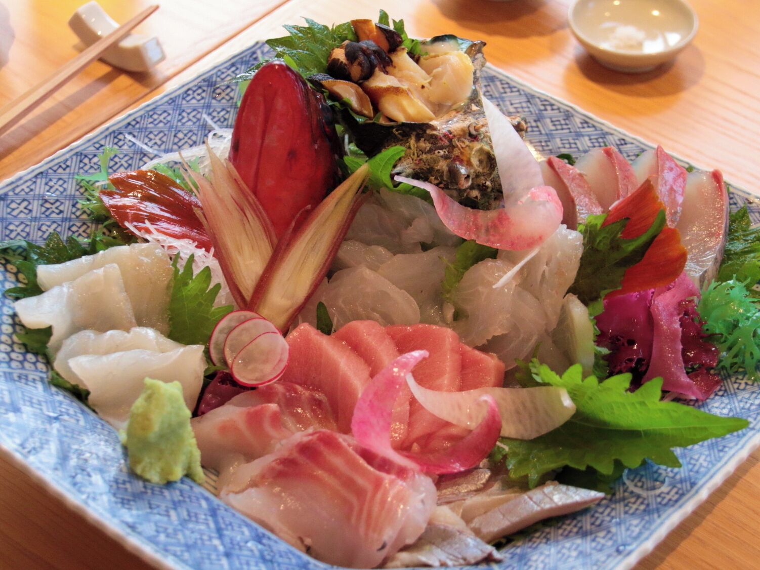 A plate of sashimi with various fish slices, radish, and green leaves.