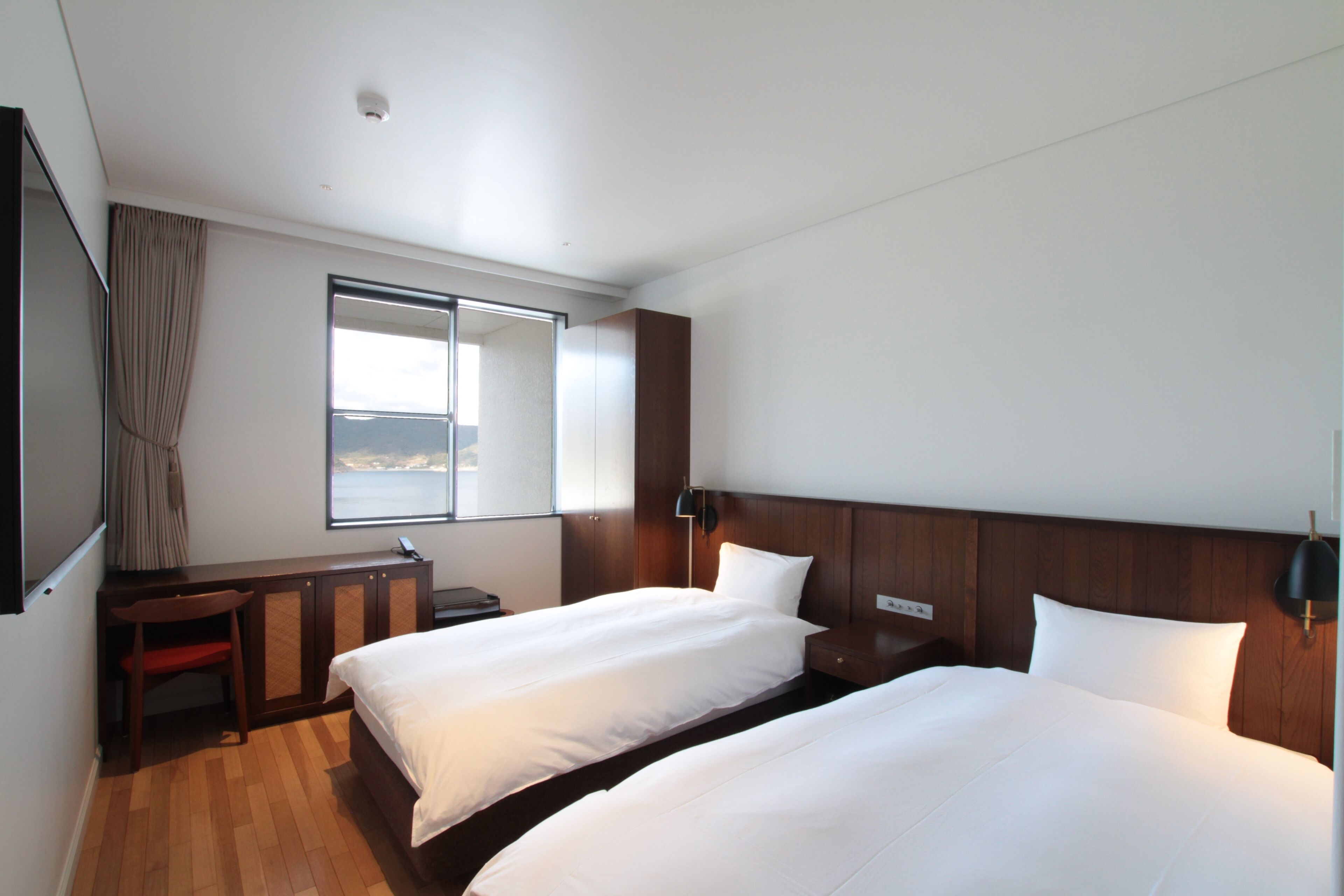 Habitación de hotel con dos camas, un escritorio, una silla, una ventana con vistas y un televisor de pantalla plana.