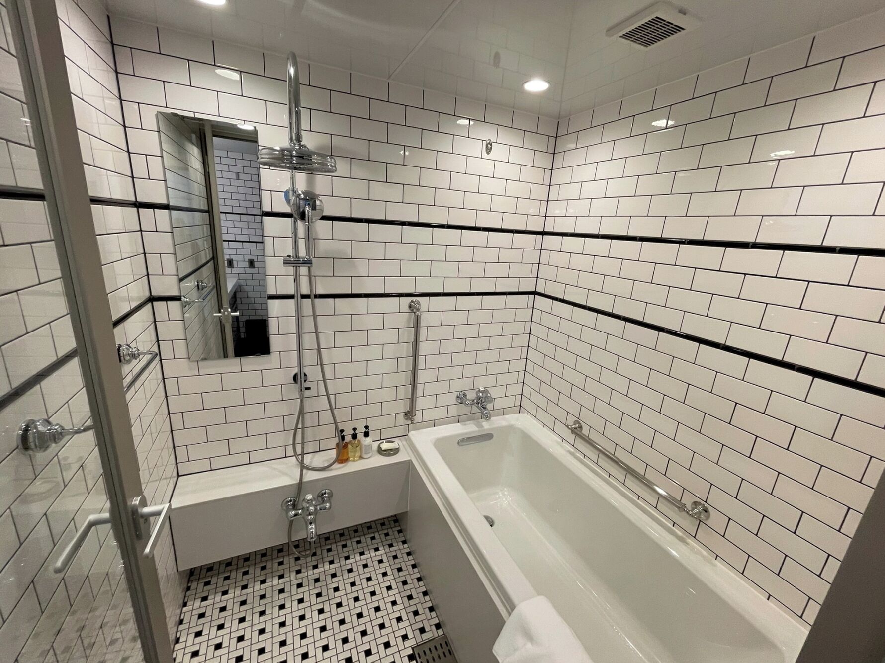 A modern bathroom with white subway tiles, a glass-enclosed shower, a white bathtub, and a black-tiled floor.