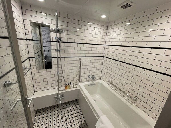 Un baño moderno con azulejos blancos tipo metro, una ducha con cerramiento de vidrio, una bañera blanca y un suelo de baldosas negras.