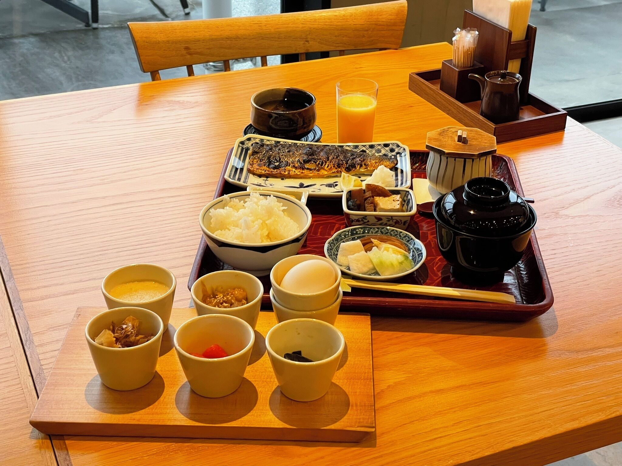 A wooden table with a tray of Japanese breakfast including rice, fish, and various side dishes.