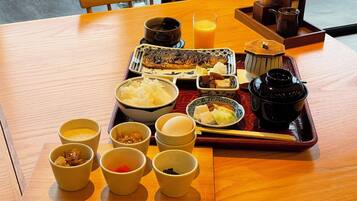 A wooden table with a tray of Japanese breakfast including rice, fish, and various side dishes.