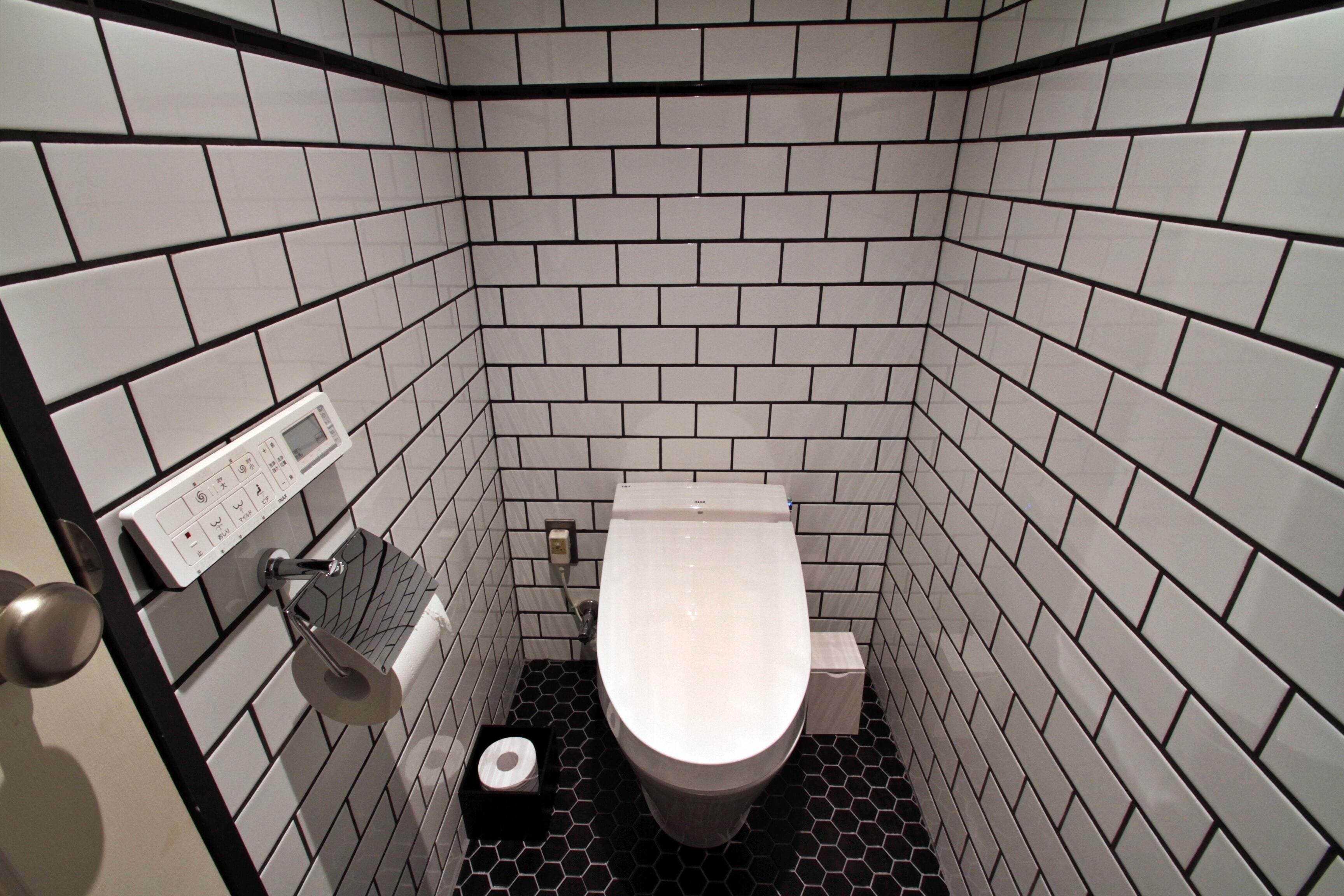 A small, modern bathroom with white and black tiles, a toilet, a hand dryer, and a paper towel dispenser.