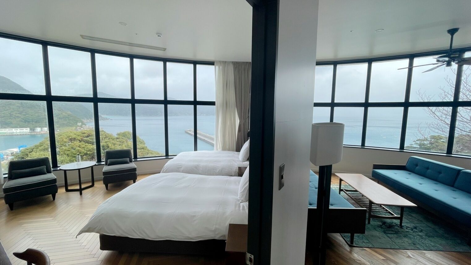 A hotel room with a large bed, a sofa, a small table, and a view of the sea.