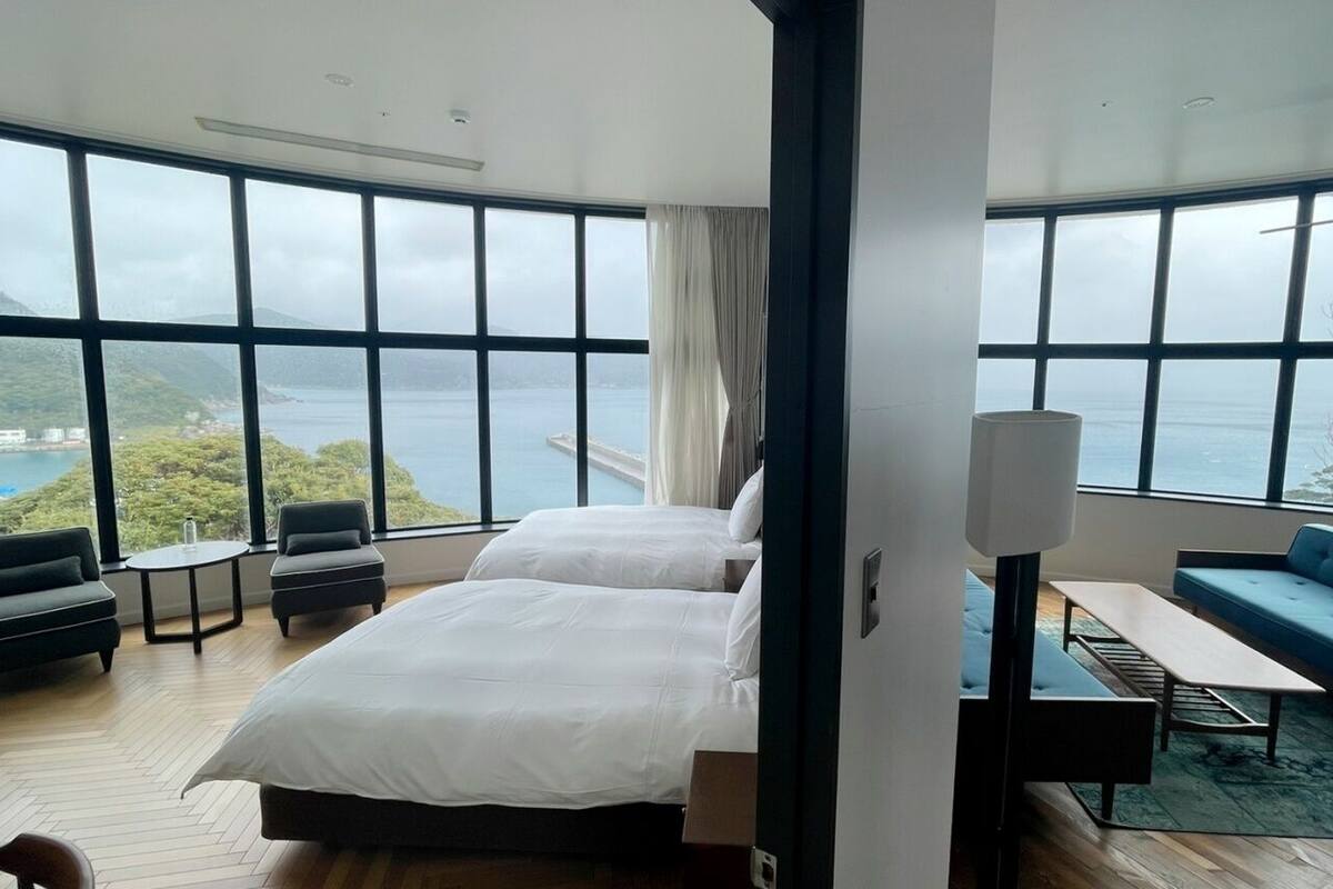 A hotel room with a large bed, a sofa, a small table, and a view of the sea.