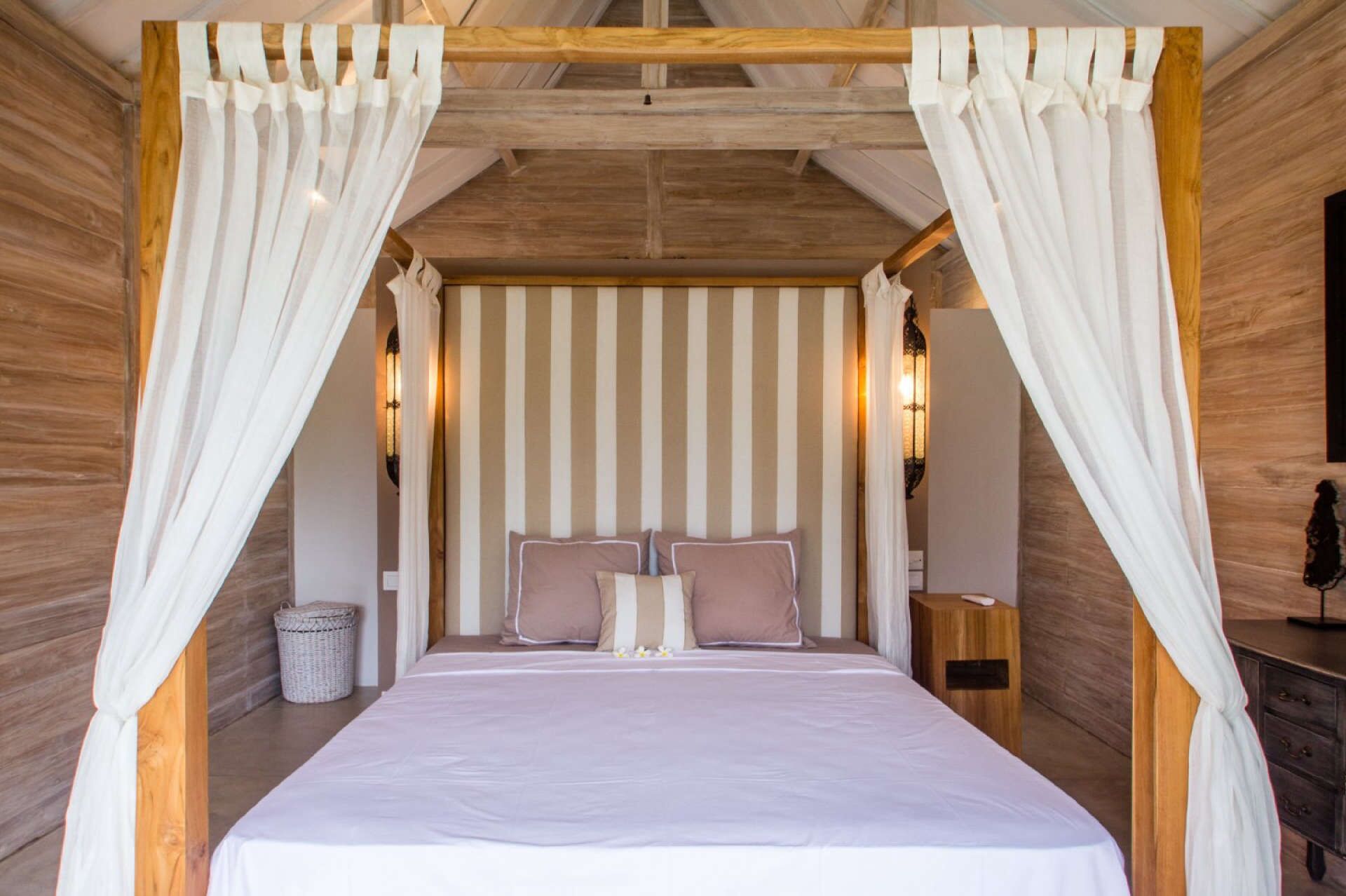 A bedroom with a canopy bed, striped wallpaper, and bedside lamps.