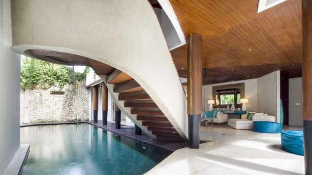 A modern interior with a curved swimming pool, a wooden staircase, and a seating area with a view of greenery outside. - Luxury Villa in Bali near Beach, Bali Villa 2003 (Seminyak)