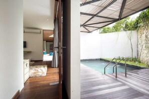 A modern interior with a wooden floor, a white sofa, and a view of a pool area with a wooden deck and metal railings.