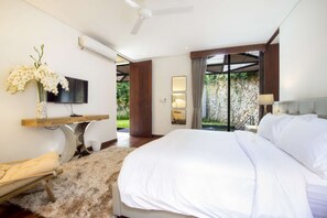 A modern bedroom with a large bed, a TV, a desk, and a view of greenery outside.