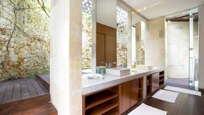 A modern bathroom with a stone wall, a wooden bench, and a large mirror. - Luxury Villa in Bali near Beach, Bali Villa 2003 (Seminyak)