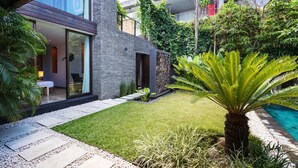 Ein modernes Haus mit Glastür, einer kleinen Terrasse mit Sitzbank und einem gepflegten Garten mit einer Palme.