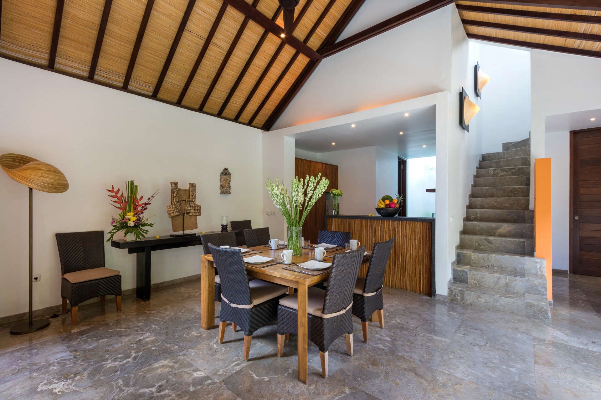 A dining area with a wooden table and chairs, a vase with flowers, and a decorative wall piece.