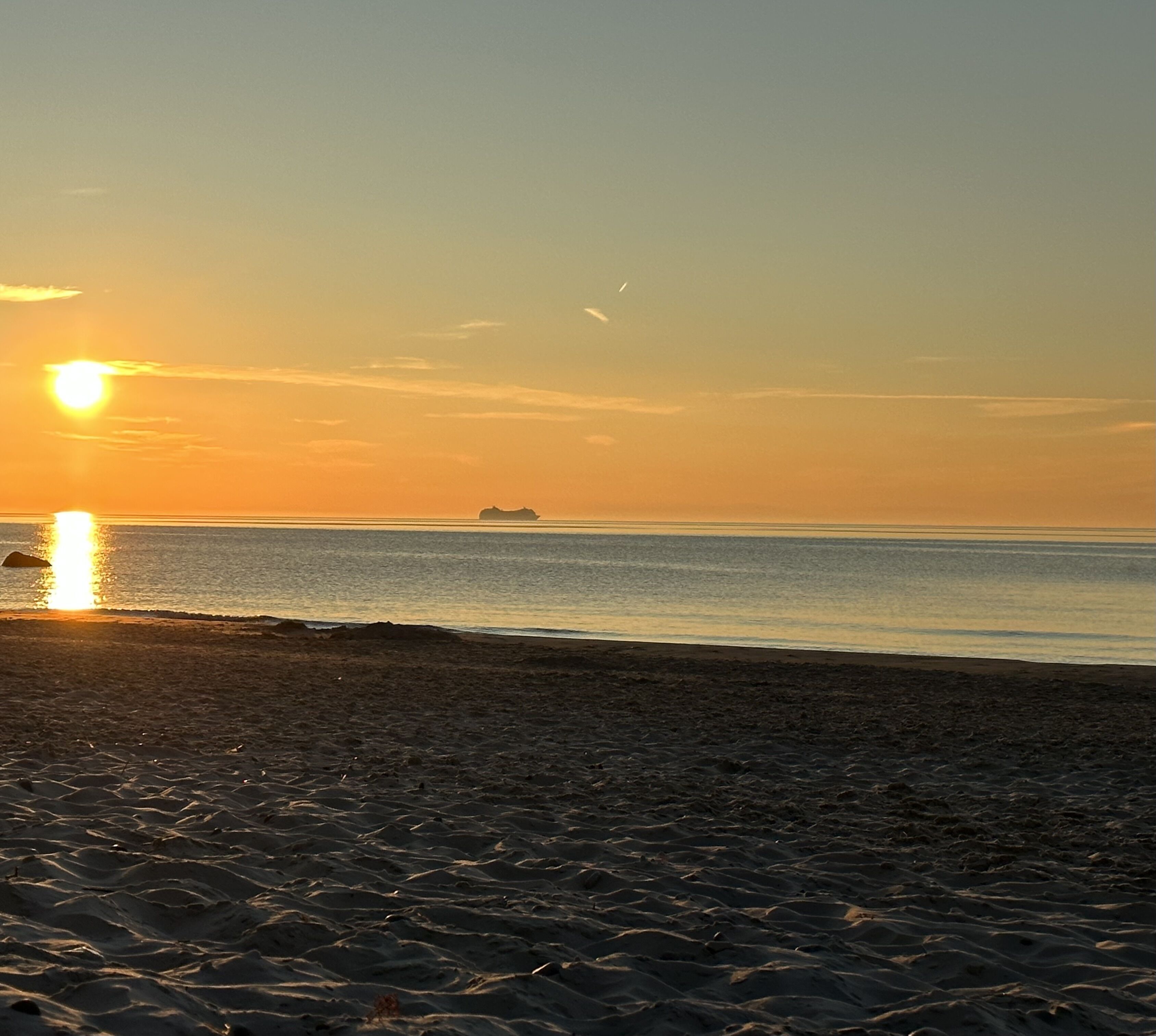 Una spiaggia con una nave all'orizzonte al tramonto.