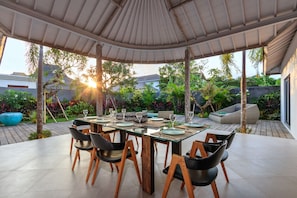 An outdoor dining area with a covered table and chairs, surrounded by lush greenery and a view of the cityscape. - Bali Villa Near the Beach, 2041 (Seminyak)