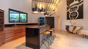 Une cuisine moderne dotée d’un îlot central, de tabourets de bar, de luminaires suspendus et d’une grande fenêtre.