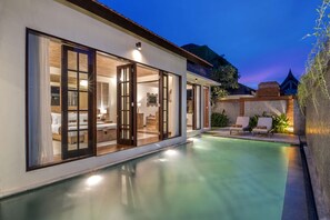 Een modern huis met een zwembad, grote schuifdeuren en een terras met loungestoelen.