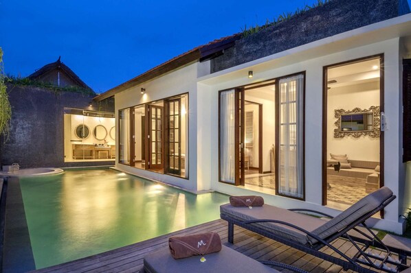 A modern villa with a swimming pool, large glass doors leading to a living area, and a stone wall.