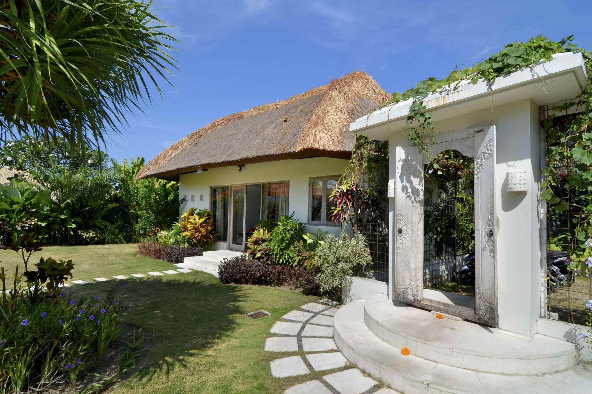 Une maison au toit de chaume, entourée d’une végétation luxuriante et d’un jardin bien entretenu.
