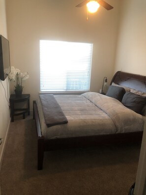 A bedroom with a bed, a bedside table, a nightstand, a window with blinds, and a ceiling fan. - Vibrant Contemporary Luxury (Charlotte)