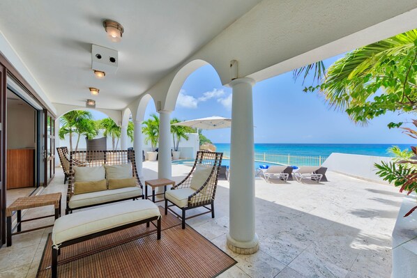 A covered outdoor seating area with a view of the ocean, featuring wicker furniture and a bamboo mat.