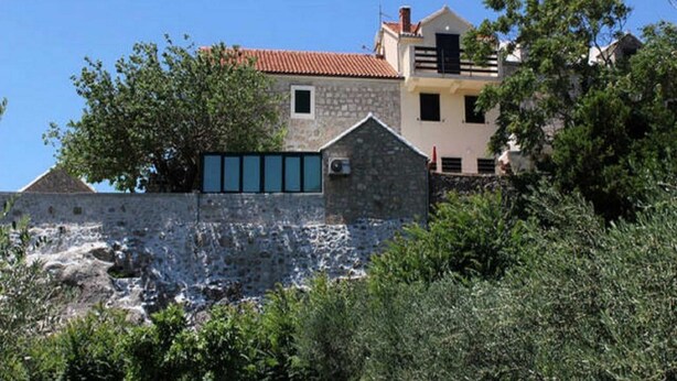 A stone building with a red-tiled roof, surrounded by greenery and a clear blue sky. - Apartments Nadia (Bol)