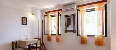 A bedroom with a bed, a table with chairs, and windows with curtains.