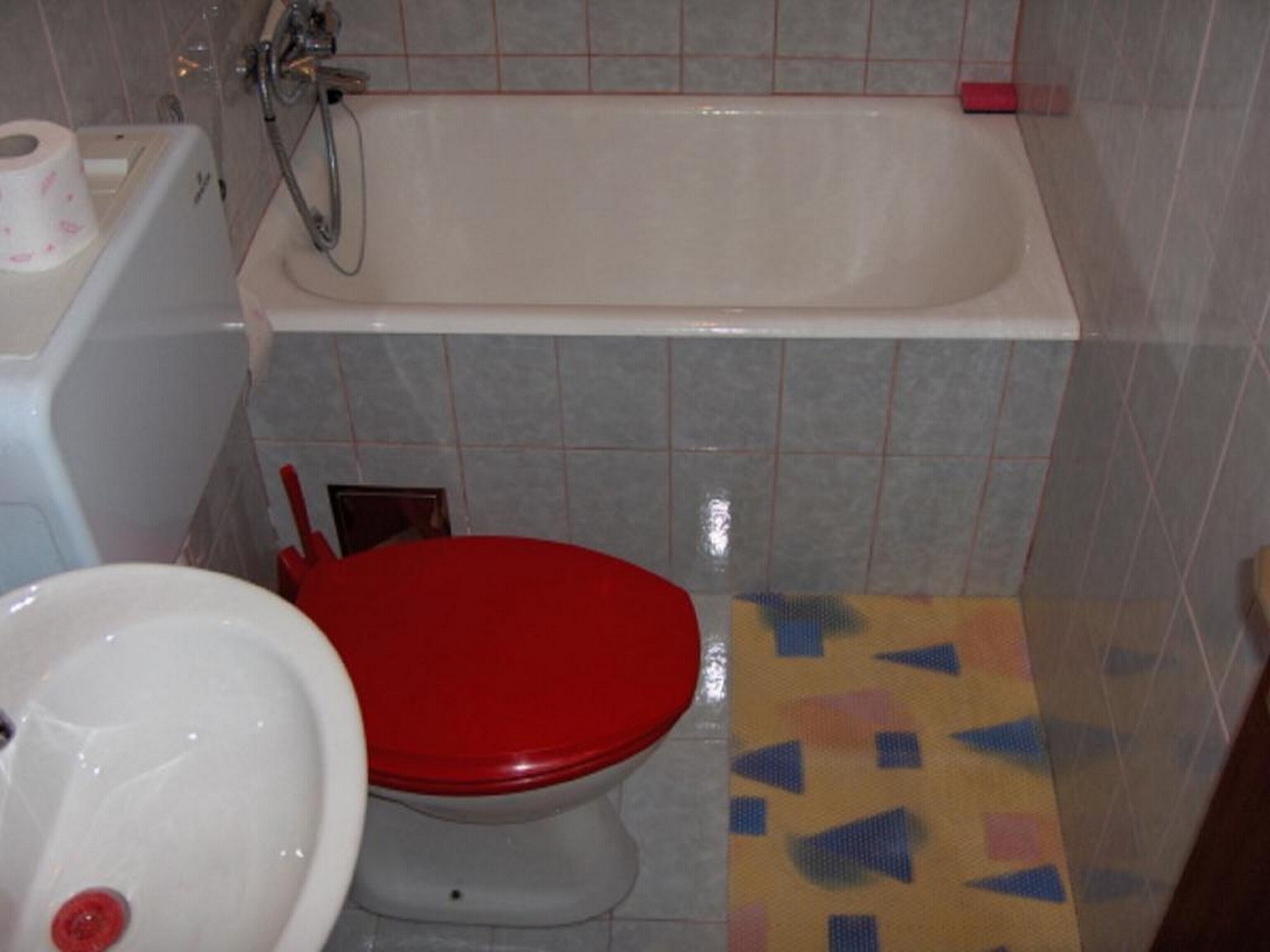 A bathroom with a red toilet, a white sink, and a bathtub.