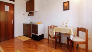 A compact kitchen with wooden cabinets, a small countertop, and a dining area with two chairs and a table. - Apartments Nadia (Bol)