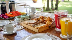 A breakfast buffet with bread, pastries, and fruit, along with cups and a juice pitcher.