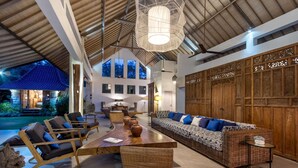 A spacious living area with a long sofa, chairs, and a dining table. There are large windows and a view of the outside. - Bali Villa Near the Beach, 2056 (Seminyak)