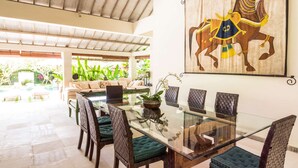A dining area with a glass table and woven chairs, a sofa, and a large horse painting on the wall. - Beautiful Villa With Private Pool, Bali Villa 2051 (Seminyak)