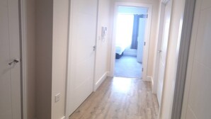A narrow hallway with white doors leading to a bedroom with a bed and a window. - Pier Apartment 3 (Gillingham)