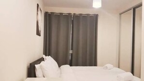 A small, neatly arranged bedroom with a bed, a bedside table, a wardrobe, and a single light fixture. - Pier Apartment 3 (Gillingham)
