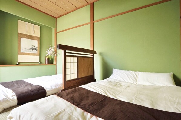 A room with two beds, green walls, wooden headboards, and a window with a plant.