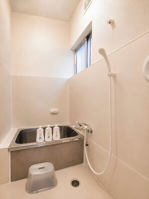 A bathroom with a shower, a sink, and three bottles of liquid soap.