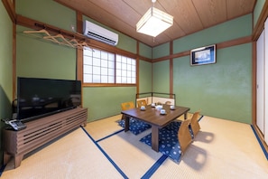 Une pièce de style japonais traditionnel, avec un sol recouvert de tatamis, une télévision, une table avec des chaises, un porte-vêtements suspendu et un tableau au mur.