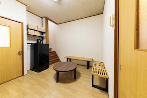 Une pièce avec un plancher en bois, une table ronde, un banc, un réfrigérateur noir et un escalier.