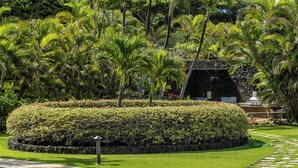 A landscaped garden with a circular hedge, a stone pathway, and palm trees. - Beachfront Wailea condo w/ ocean views and lanai (Wailea)