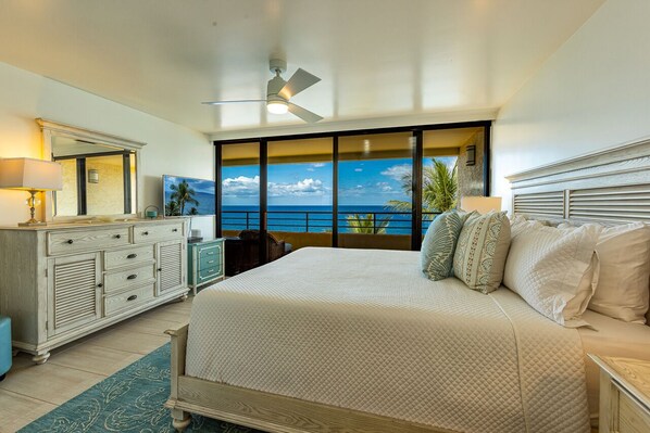 A bedroom with a large bed, a dresser, a nightstand, a ceiling fan, and a view of the ocean.