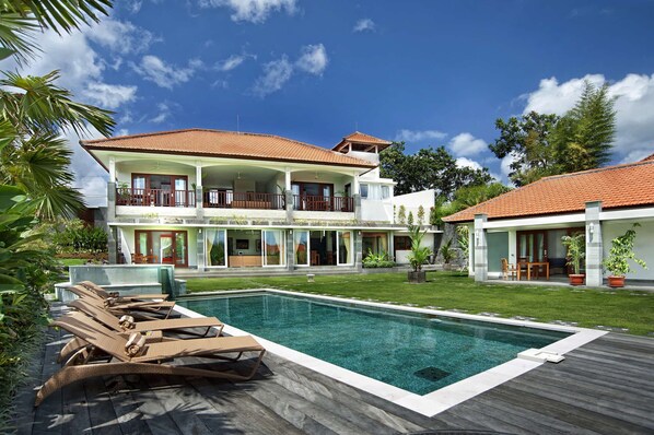 A two-story house with a swimming pool, a balcony, and a garden.