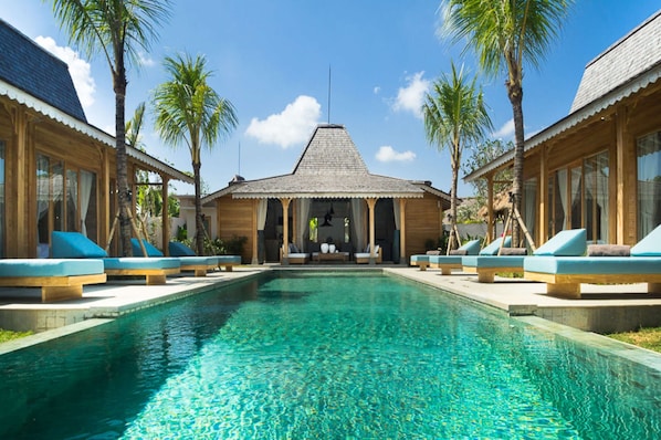 A pool area with lounge chairs and a building with a thatched roof.