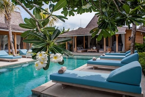 A poolside area with lounge chairs, a pool, and a covered seating area with a view of the pool.