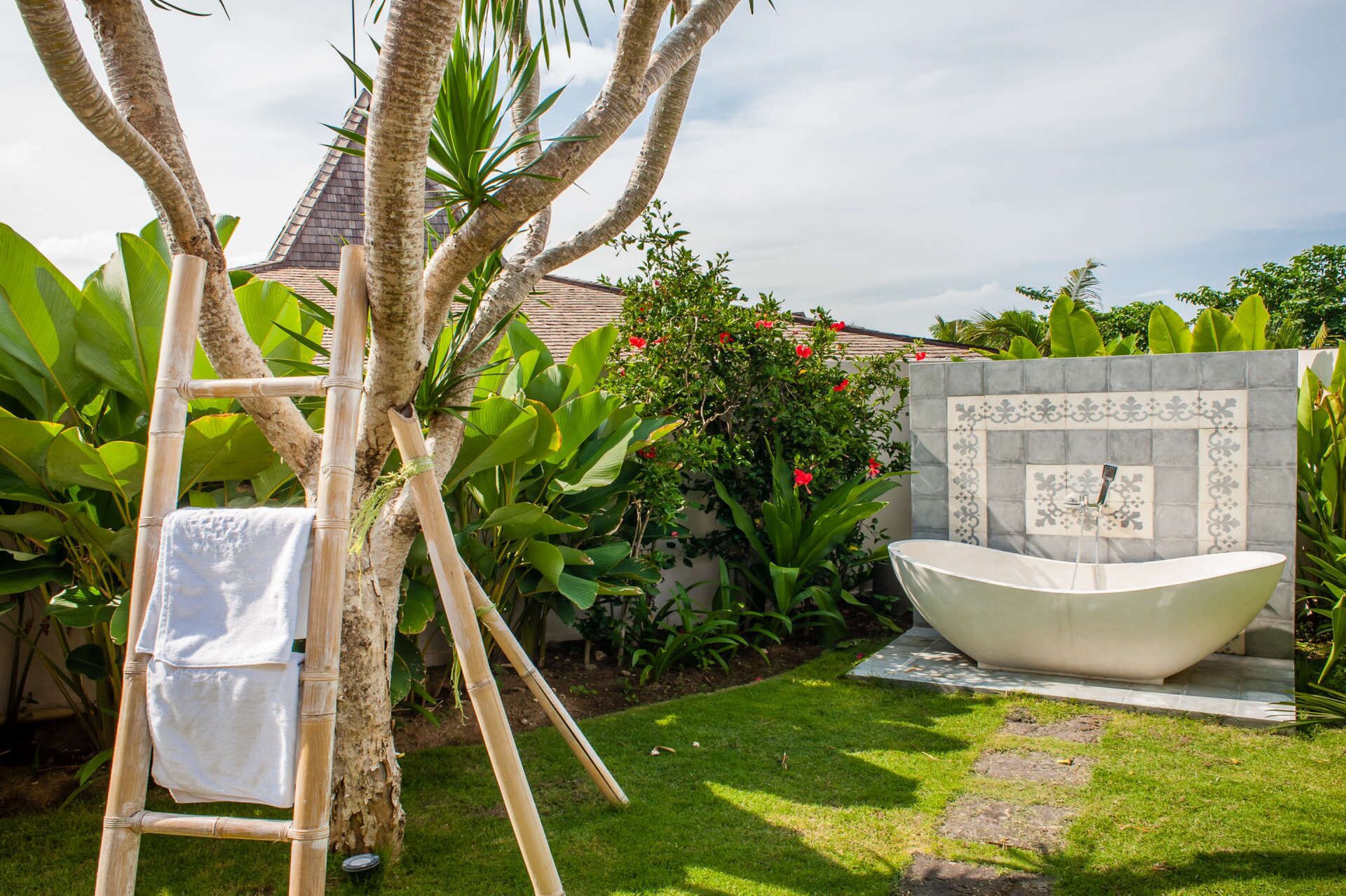A garden with a large white bathtub, a bamboo ladder, and lush greenery.