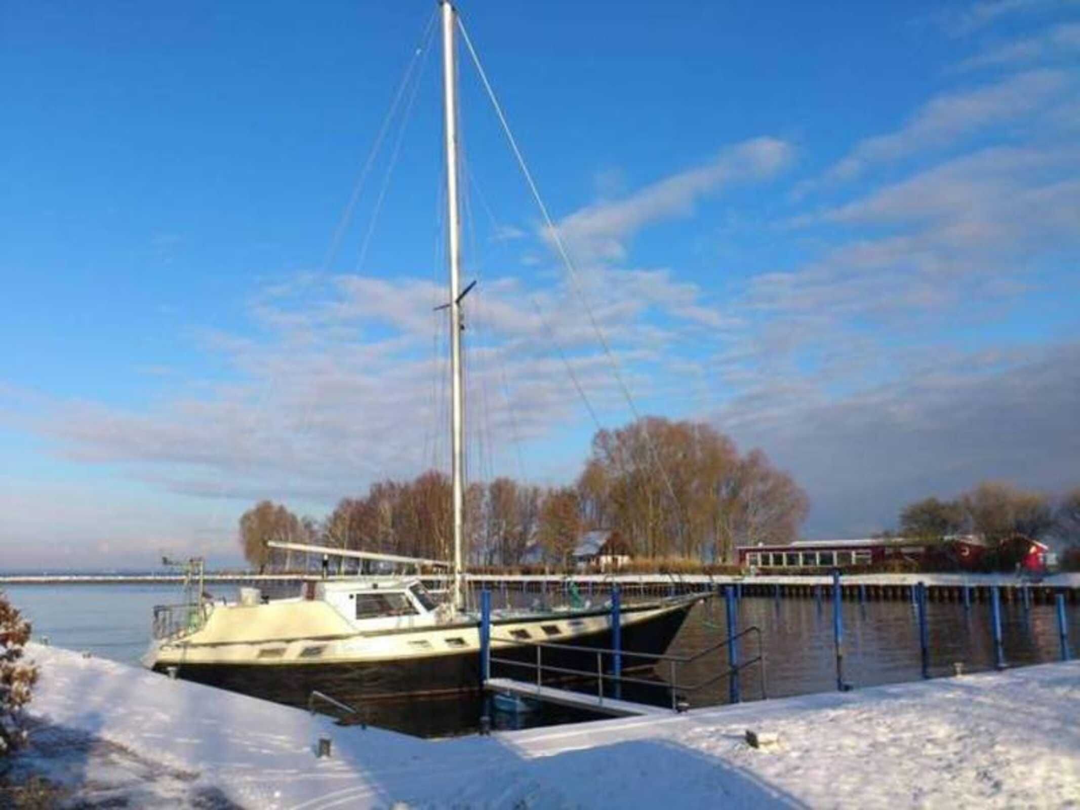 A docked sailboat at a marina with a clear sky and trees in the background.